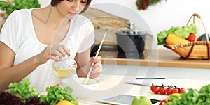 Beautiful Hispanic woman cooking in kitchen while using tablet computer and wooden spoon. Housewife found new recipe for