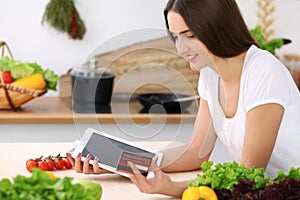 Beautiful Hispanic woman cooking while using tablet computer in kitchen or making online shopping by touchpad and credit