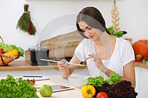 Beautiful Hispanic woman cooking while using tablet computer in kitchen or making online shopping by touchpad and credit