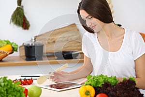 Beautiful Hispanic woman cooking while using tablet computer in kitchen or making online shopping by touchpad and credit