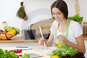 Beautiful Hispanic woman cooking while using tablet computer in kitchen or making online shopping by touchpad and credit