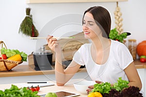 Beautiful Hispanic woman cooking while using tablet computer in kitchen or making online shopping by touchpad and credit