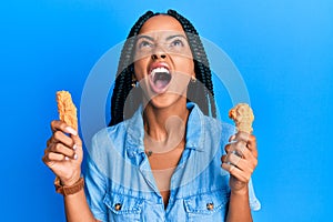 Beautiful hispanic woman eating chicken wings angry and mad screaming frustrated and furious, shouting with anger looking up