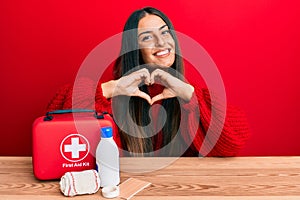 Beautiful hispanic woman with first aid kit smiling in love doing heart symbol shape with hands