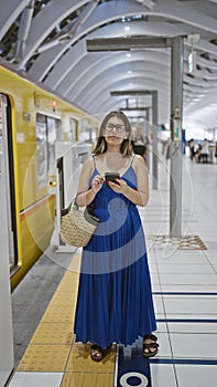 Beautiful hispanic woman in glasses, engrossed on phone, awaiting her subway journey at ginza station amidst bustling city life