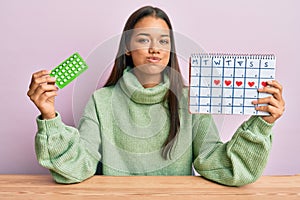 Beautiful hispanic woman holding birth control pills puffing cheeks with funny face
