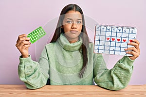 Beautiful hispanic woman holding birth control pills relaxed with serious expression on face