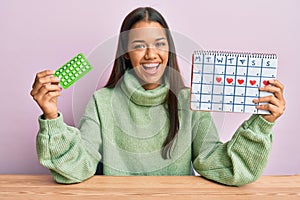 Beautiful hispanic woman holding birth control pills smiling and laughing hard out loud because funny crazy joke