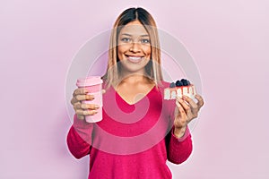 Beautiful hispanic woman holding takeaway cup of coffee and cheesecake smiling with a happy and cool smile on face