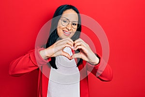 Beautiful hispanic woman with nose piercing wearing casual look and glasses smiling in love doing heart symbol shape with hands