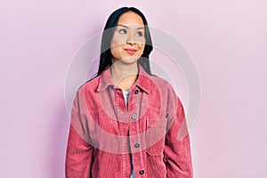 Beautiful hispanic woman with nose piercing wearing casual pink jacket smiling looking to the side and staring away thinking