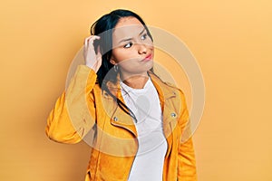 Beautiful hispanic woman with nose piercing wearing yellow leather jacket confuse and wondering about question