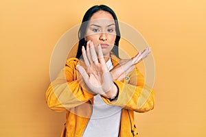 Beautiful hispanic woman with nose piercing wearing yellow leather jacket rejection expression crossing arms doing negative sign,
