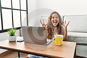 Beautiful hispanic woman using computer laptop at home celebrating victory with happy smile and winner expression with raised