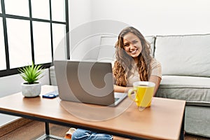 Beautiful hispanic woman using computer laptop at home happy face smiling with crossed arms looking at the camera