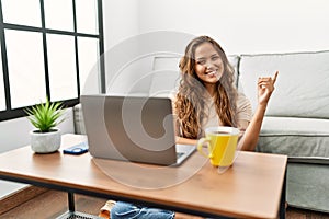 Beautiful hispanic woman using computer laptop at home smiling happy pointing with hand and finger to the side