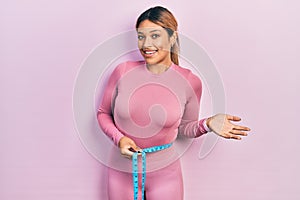 Beautiful hispanic woman using tape measure measuring waist celebrating achievement with happy smile and winner expression with