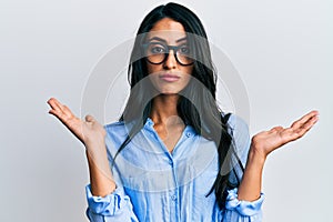 Beautiful hispanic woman wearing business clothes and glasses clueless and confused with open arms, no idea and doubtful face