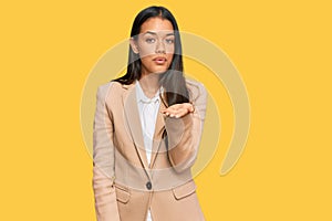 Beautiful hispanic woman wearing business jacket looking at the camera blowing a kiss with hand on air being lovely and sexy