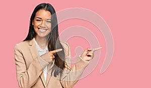 Beautiful hispanic woman wearing business jacket smiling and looking at the camera pointing with two hands and fingers to the side