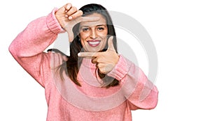 Beautiful hispanic woman wearing casual winter sweater smiling making frame with hands and fingers with happy face