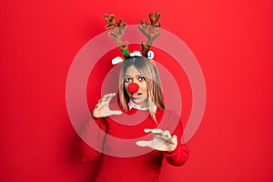 Beautiful hispanic woman wearing deer christmas hat and red nose afraid and terrified with fear expression stop gesture with