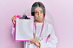 Beautiful hispanic woman wearing doctor stethoscope holding clipboard depressed and worry for distress, crying angry and afraid