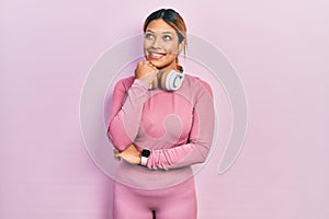 Beautiful hispanic woman wearing gym clothes and using headphones with hand on chin thinking about question, pensive expression