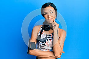 Beautiful hispanic woman wearing gym clothes and using headphones thinking concentrated about doubt with finger on chin and