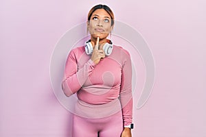 Beautiful hispanic woman wearing gym clothes and using headphones thinking concentrated about doubt with finger on chin and