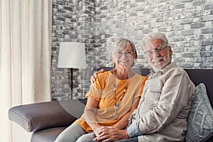 Beautiful hoary good-looking mature spouses relaxing together on comfy couch at modern home smiling staring at camera feel