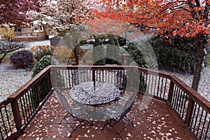 Beautiful Home Backyard Deck Covered in a Light Dusting of Snow during Autumn with a Table and Chairs and Colorful Trees