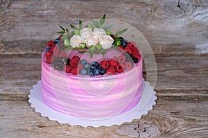 Beautiful home cake with pink and purple cream, decorated with white roses and berries of BlackBerry, blueberries, raspberries