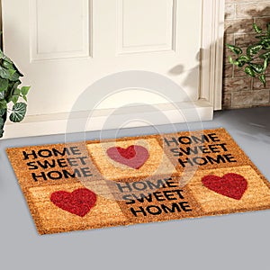 Beautiful Home sweet home peach color coir doormat with hearts Placed outside door with yellow flowers and green leaves