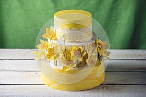 Beautiful home yellow wedding three-tiered cake decorated with red spring flowers. Concept floral trends in desserts