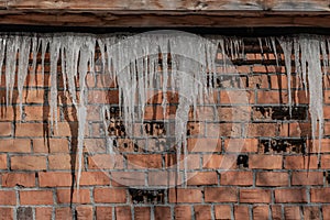 A beautiful horizontal texture of part of a old crashed brick wall in orange hue with a group of sharp white icicles is hanging do