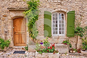 A beautiful house facade in Provence, with a wooden door and French window with green shutters.