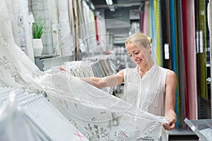 Beautiful housewife buying white curtains in home decor furnishings store.