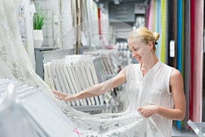 Beautiful housewife buying white curtains in home decor furnishings store.