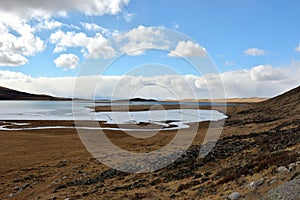 A beautiful huge lake captured by the first ice in the valley at the foot of a gently sloping mountain on a sunny day