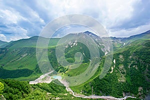 Beautiful huge mountains peaks in snow, blue sky, white clouds, blue lake at the foot of the mountain, green hills, green valley