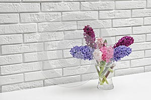 Beautiful hyacinths in glass vase on table against brick wall, space for text