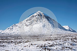 Beautiful iconic landscape Winter image of Stob Dearg Buachaille Etive Mor mountain in Scottish Highlands againstd vibrant blue