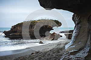 Beautiful image of a beach with a rock formation in the middle taken on a cloudy winter day at Truman Track, New Zealand