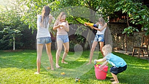 Beautiful image of happy laughing family with children having fun at hot summer day with water guns and garden hose