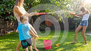 Beautiful image of happy laughing family with children having fun at hot summer day with water guns and garden hose