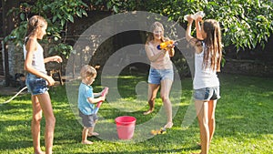 Beautiful image of happy laughing family with children having fun at hot summer day with water guns and garden hose