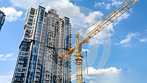 Beautiful image of high yellow building crane on construction site against high modern building made of concrete and