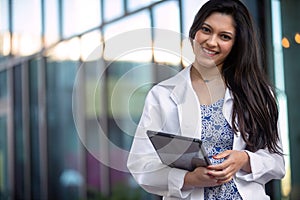 Beautiful Indian American woman in a lab coat, white robe with electronic tablet, medical professional smiling portrait