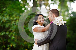 Beautiful indian bride and caucasian groom, in summer park. Happy young woman holding flowers. Young man smiling, Couple